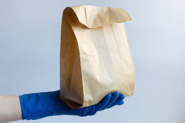 男性的手上戴着防护手套，拿着装着食物的纸袋。食品运送，食品捐赠。冠状病毒隔离。图片下载