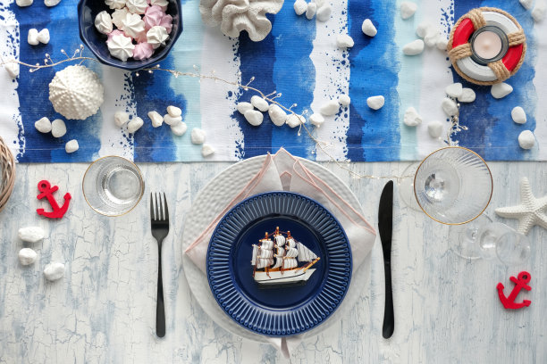 哥伦布日餐桌设置与航海海洋装饰在蓝色和白色条纹runner，经典的蓝白色盘子，餐具在白色质朴的桌子。俯视图，休闲现代午餐。图片下载