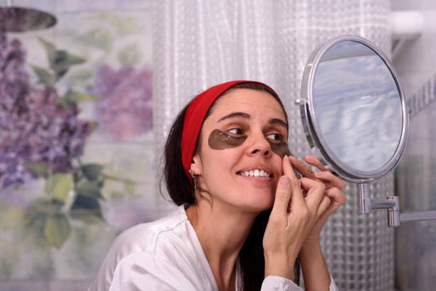 漂亮的褐发女人穿着睡衣在家。她做美容手术，用眼罩遮住眼睛。生活保健概念图片下载