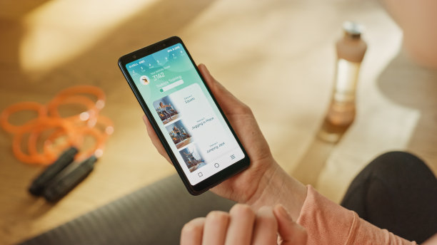 过肩镜头:健康女性拿着智能手机，使用健身追踪应用程序，查看优质健身视频。模拟培训应用软件图片下载