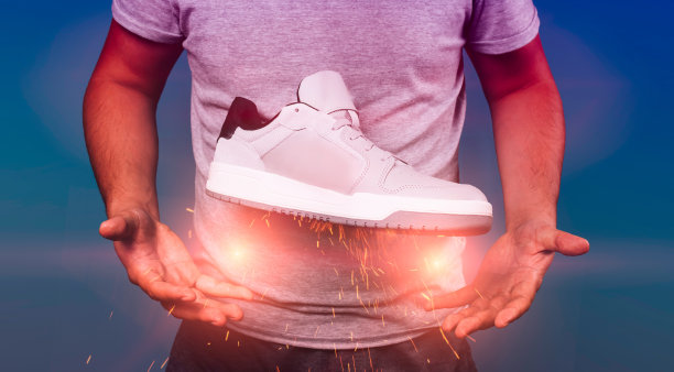 男人捧着时髦的灰色运动鞋在空中，手下靴子，运动的生活方式，呈现新型的鞋子图片下载