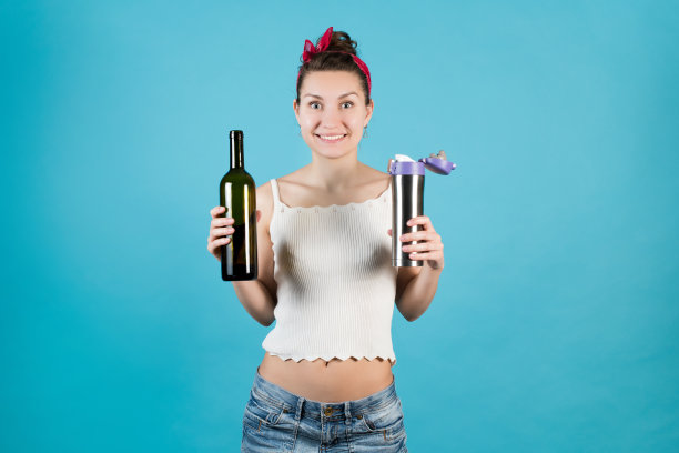 笑容灿烂的女孩拿着一个热水瓶和一瓶酒在蓝色的背景图片下载