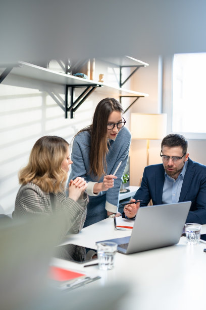 同事和客户用笔记本电脑和平板电脑谈论策略。在创意办公室里，高效的同事们站在公司会议桌前。团队合作与社会观念图片下载