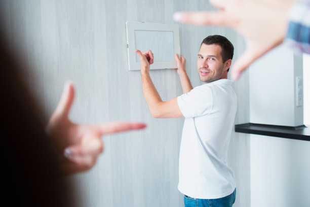 一对夫妇搬进了新房。在装饰新公寓时女性手的特写照片，男人在墙上挂照片或相框图片下载