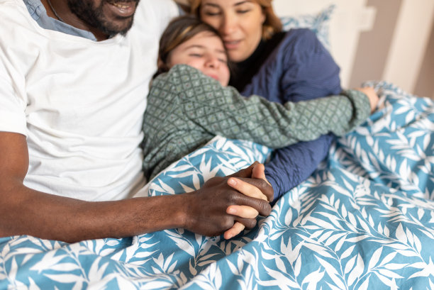 幸福的混血家庭拥抱着，白人妈妈和非洲人爸爸温柔地拥抱着刚睡醒的女儿，专注于黑白手指交错的细节图片下载