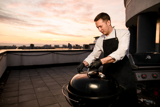 男厨师准备烧烤设备。傍晚的天空在背景。图片下载