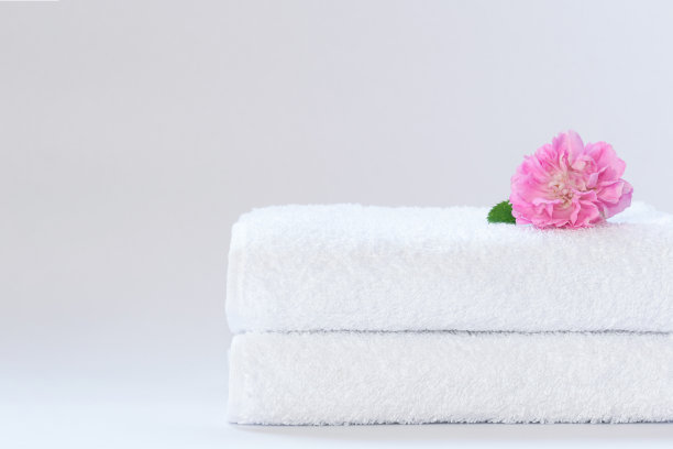 两张折叠整齐的白色毛巾布毛巾，在浅色背景上放一朵玫瑰花。图片下载