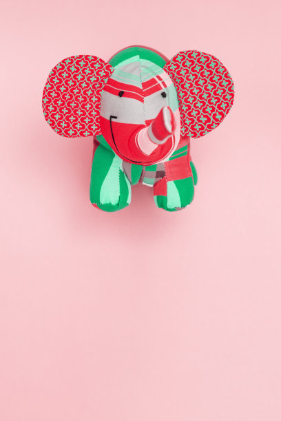 柔软的玩具大象，鲜艳的彩色纺织玩具在粉红色的纸背景与复制空间。为孩子或装饰手工制作的东西。垂直格式。图片下载
