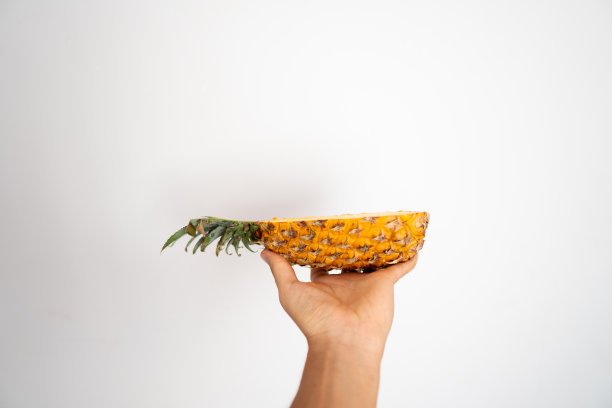 女人的手拿着半个成熟的菠萝在一个白色的背景。图片下载