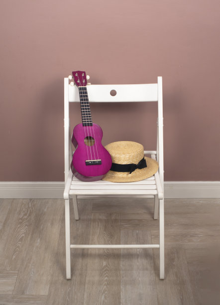 白色的木椅上放着粉红色的尤克里里琴和带黑丝带的草帽图片下载