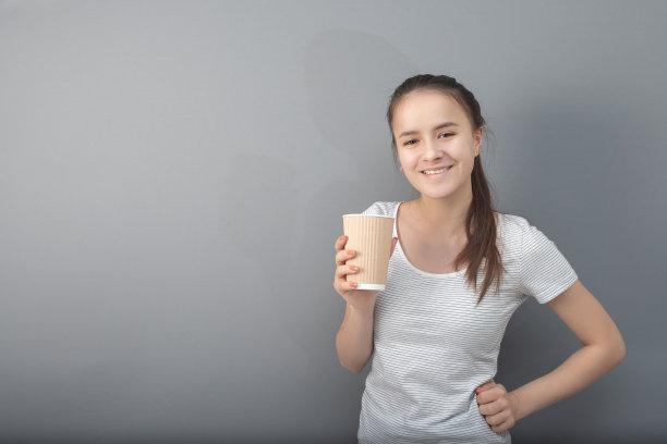一杯芳香的咖啡。年轻女子在灰色背景下喝热饮图片下载