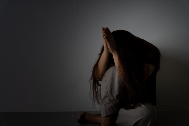 悲伤的女人抱着膝盖独自坐在黑暗的房间里哭泣。抑郁，不快乐，紧张和焦虑障碍的概念。图片下载