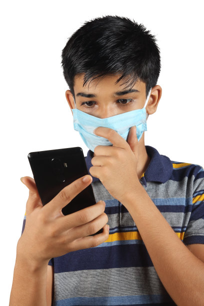 印度小男孩使用手机和戴口罩抗击新冠肺炎的肖像图片下载
