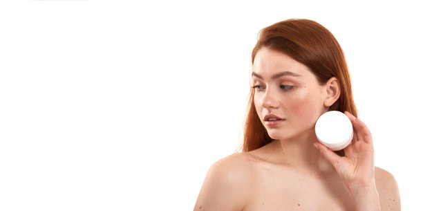 非常适合她敏感的皮肤。年轻迷人的红发女孩与雀斑展示化妆品，而站在工作室的白色背景图片下载