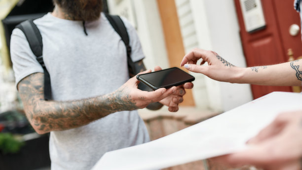 这是一名留着胡子、头戴头盔、背着背包的快递员用智能手机送餐的照片，信封里是一位女顾客。快递、派送的服务理念图片下载