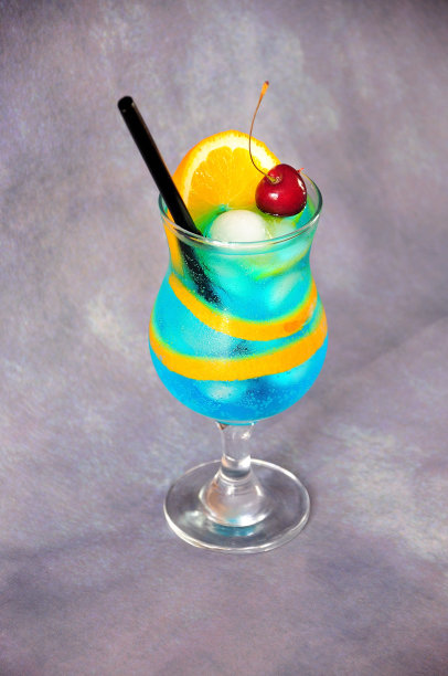 高脚杯，配上莫吉托鸡尾酒，上面有吸管、樱桃、冰块和一片橙子，背景是灰色的。图片下载