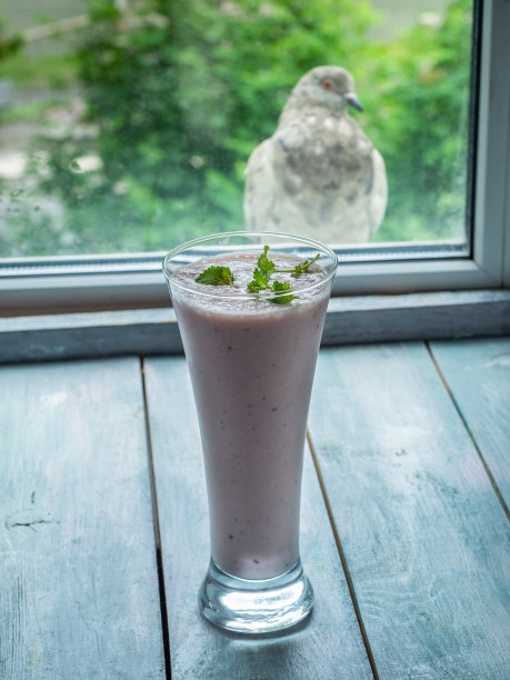 牛奶和水果鸡尾酒在一个小点心高脚杯，站在一个木制的桌子上与绿树窗外的近景图片下载