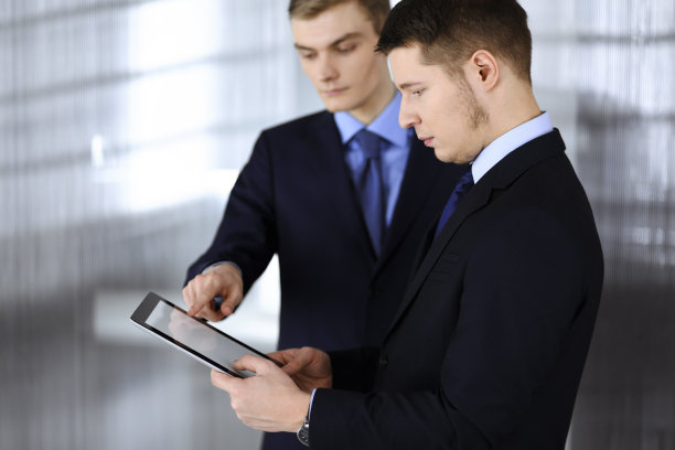 商务人士，站在现代办公室里使用平板电脑。一个不知名的商人和一个同事在工作。团队合作和伙伴关系概念图片下载