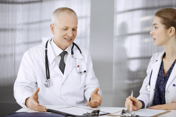 年长的医生和他的女同事讨论当前的疾病治疗，而坐在工作地点在诊所。团队合作在医院。医疗保健理念图片下载