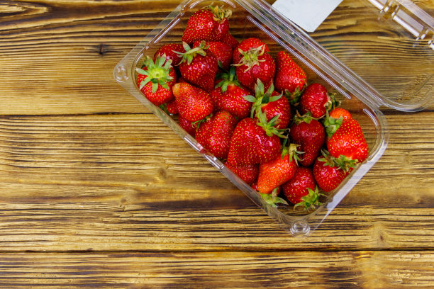 新鲜草莓装在塑料盒里放在木桌上。俯视图图片下载