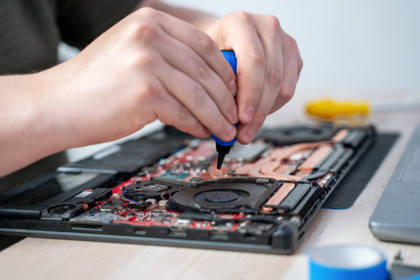 一名男子用一种专用的吹灰工具清理笔记本电脑。笔记本冷却系统冷却器上有灰尘。维修和服务笔记本电脑和个人电脑。图片下载