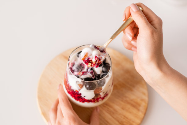 女孩手拿一茶匙新鲜可口的自制酸奶倒在杯子上图片下载