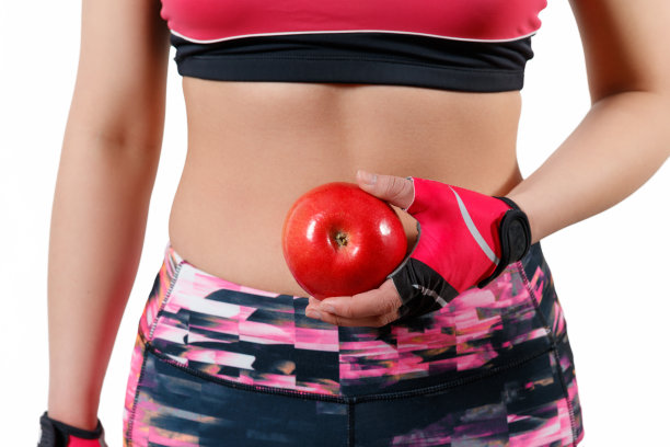 苗条的运动员的身材，一个年轻的女孩在紧身的衣服为健身。在他的手中拿着一个大的红苹果在白色的背景孤立图片下载