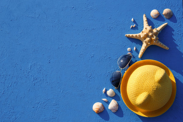 以海洋主题的沙滩饰品为框架:黄色草帽、太阳镜、海星和贝壳在蓝色背景上。图片下载