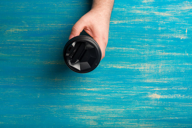 一次性纸杯咖啡在一个男性的手在一个蓝色的木制背景。图片下载