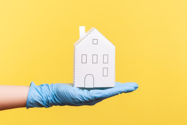 侧面特写人类手在蓝色的外科手套拿着白纸房子外观在手里。图片下载