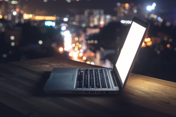 桌上的笔记本电脑，以城市夜晚为背景图片下载