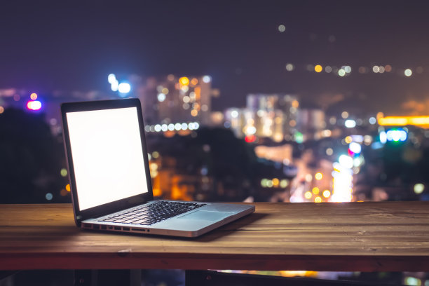 桌上的笔记本电脑，以城市夜晚为背景图片下载