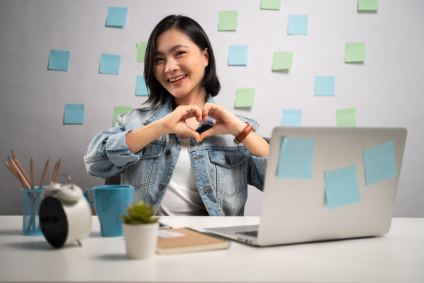 亚洲女性在爱的快乐工作在笔记本电脑显示我爱你的签名在家里办公室。亲密。居家办公COVID-19概念。图片下载