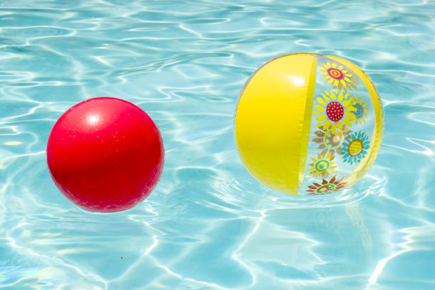 明亮的黄色花沙滩球和红色球在水晶清澈的蓝色水面反射阳光图片下载
