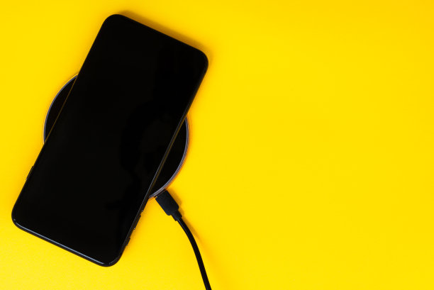 黑色手机正在无线充电，黄色背景。现代电子产品的概念。水平位置，闭合，平铺，复制空间。图片下载