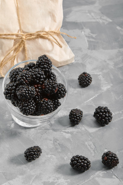 一个装满黑莓的小玻璃杯。特写，成熟的黑莓莓在灰色的背景发货产品，副本空间，照片为商店的目录图片下载