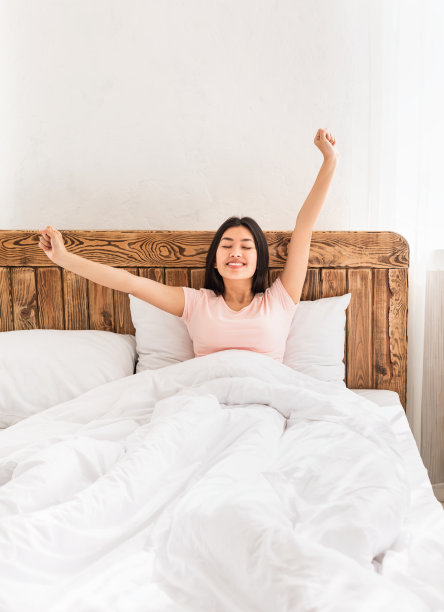 中国女孩在室内的床上伸开双手醒来，是垂直的图片下载