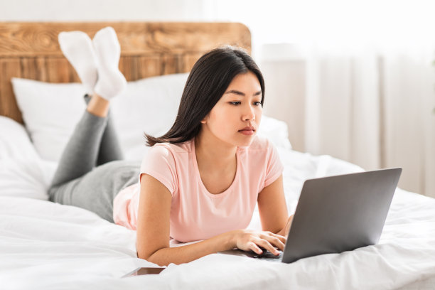 亚洲妇女拿着笔记本电脑远远地躺在室内的床上工作图片下载