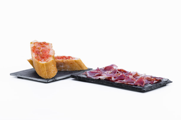 典型的西班牙火腿放在深色的盘子里，旁边是涂了番茄的面包片放在深色的盘子里图片下载