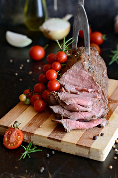 在木板上切一片香料烤牛肉，配上一小枝樱桃番茄和新鲜迷迭香。多汁烤肉(烤牛肉)。图片下载