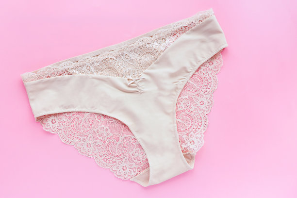 浅粉色背景的米色蕾丝女性内裤。图片下载