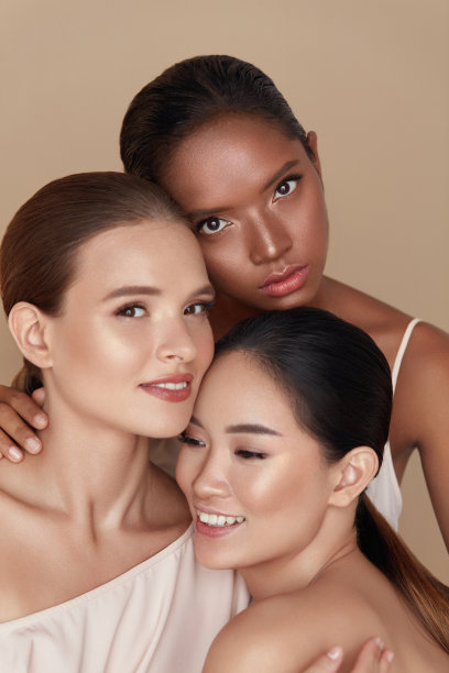 多样化。美丽的肖像模型。民族妇女与化妆和容光焕发的皮肤站在一起对米色背景。白人，亚洲和混合种族女性拥抱和看着镜头。图片下载