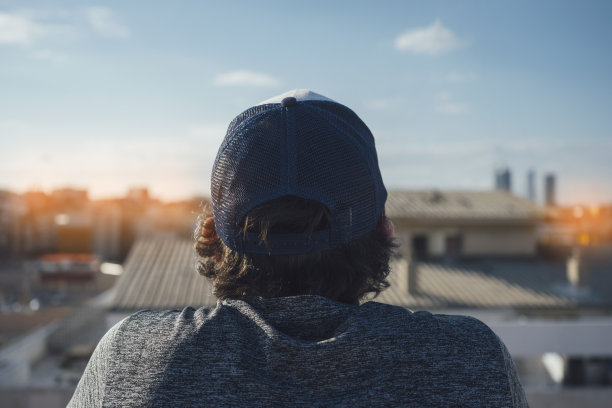 这张照片是从后面拍的一个男孩戴着长头发的帽子。从建筑物的屋顶看这个城市图片下载