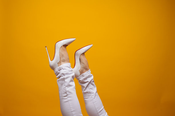 女性脚在美丽的白色细高跟鞋，黄色的背景拷贝空间。图片下载