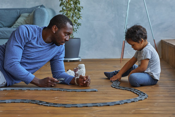 非洲家庭的父亲和蹒跚学步的孩子男孩有乐趣在温暖的地板在家里玩玩具火车集图片下载