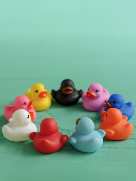 一群五颜六色的橡皮鸭子围成一圈坐在一张旧木绿松石色的桌子上。图片下载