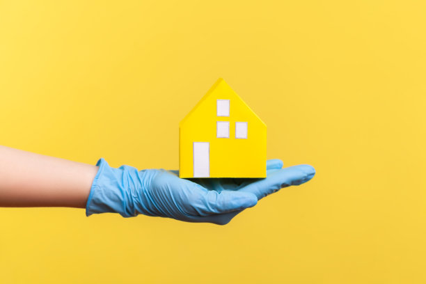 侧面特写人类手在蓝色的外科手套拿着黄色的纸房子外观在手里。图片下载