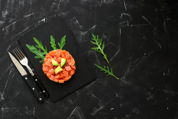 新鲜的三文鱼、鳄梨和芝麻菜沙拉放在一个烹饪圈里的石板盘子上，黑色的混凝土背景。生三文鱼鞑靼。俯视图，平放，复制空间。图片下载