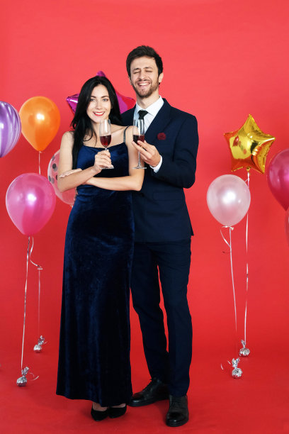 甜蜜的情侣爱的微笑，在圣诞节的时候喝葡萄酒，在红色的背景下庆祝新年，情人节图片下载