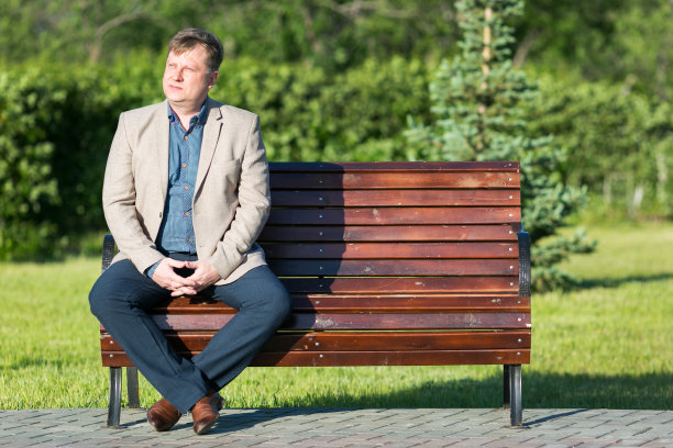 金发的成年男子正坐在公园的长椅上。图片下载